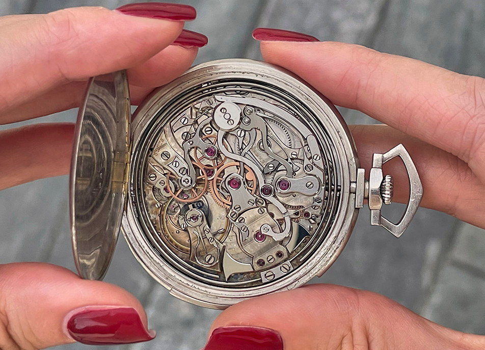 Zwei Haende halten eine geoeffnete Taschenuhr, das Uhrwerk liegt frei